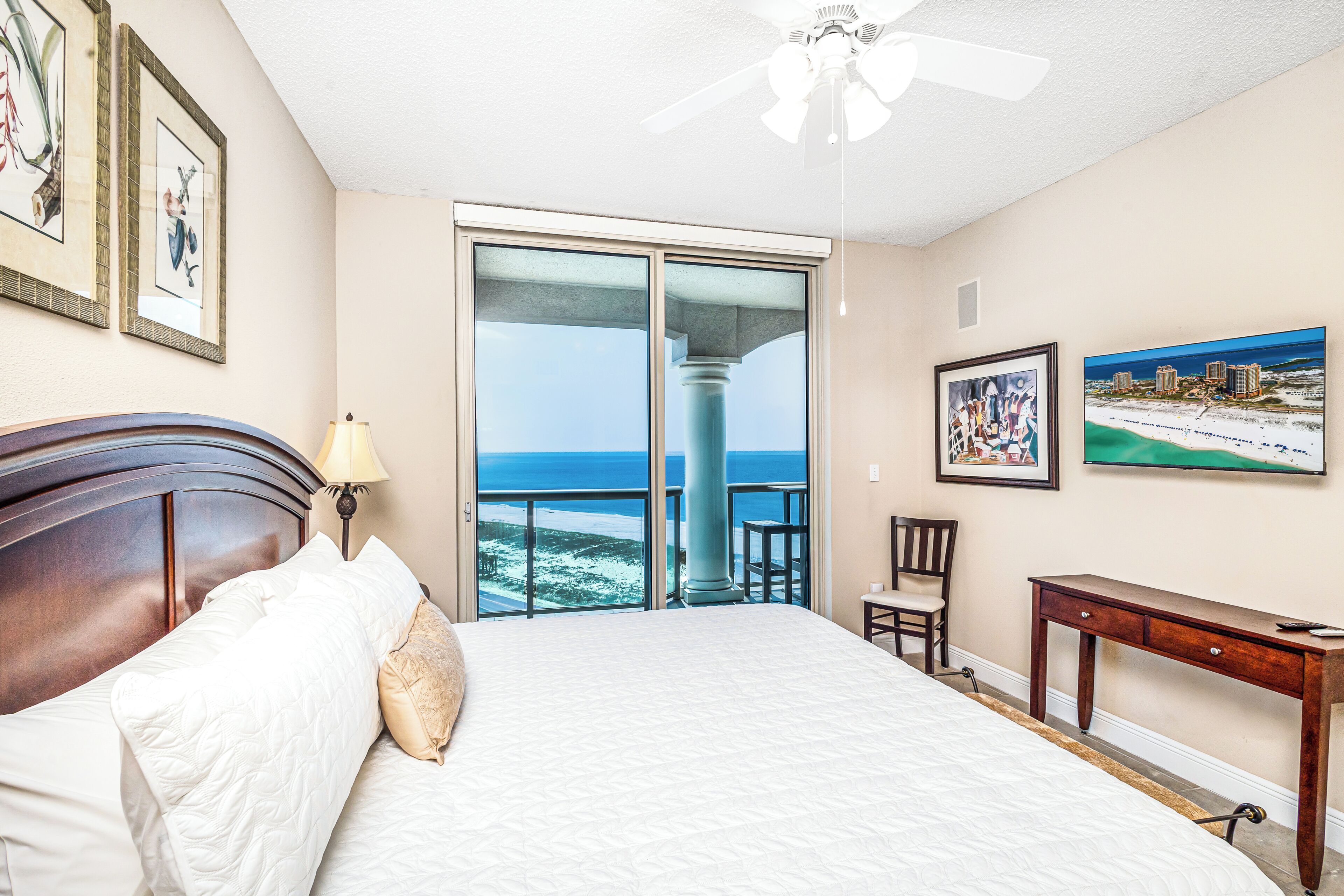 Quarto de hotel com cama, escrivaninha, cadeira e varanda com vista para o mar.