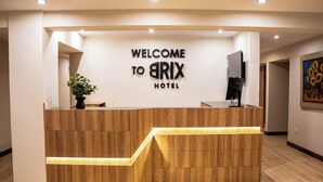 Una recepción con un cartel de 'WELCOME TO ARIX HOTEL', una planta en maceta y un televisor de pantalla plana.