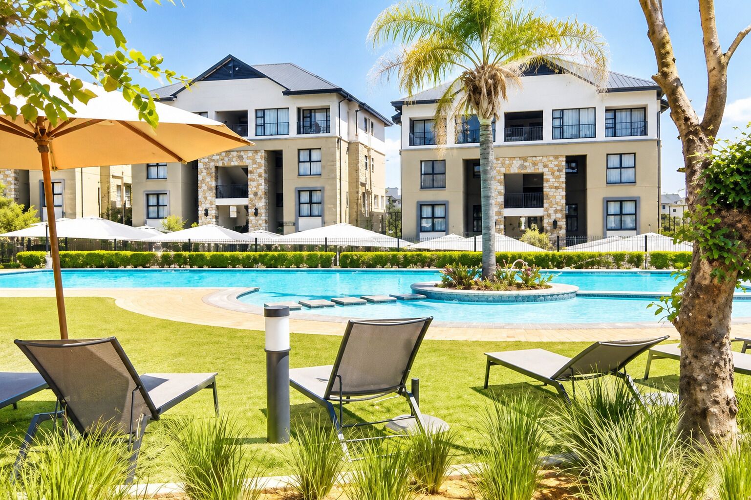 A pool area with lounge chairs and umbrellas, surrounded by multi-story buildings with balconies.