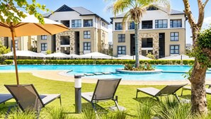 A pool area with lounge chairs and umbrellas, surrounded by multi-story buildings with balconies. - Lovely 1-bedroom apartment in Waterfall Midrand. (Waterfall, Midrand)