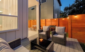 A patio with wicker furniture, a table with a candle, and a wooden fence. - Luxury New Build with 2 Ensuite Suites & Private Backyard Near UT & Downtown (Austin)