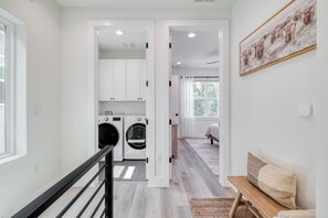 A laundry area with a washing machine and dryer, a bench with a cushion, and a framed picture on the wall. - Luxury New Build with 2 Ensuite Suites & Private Backyard Near UT & Downtown (Austin)