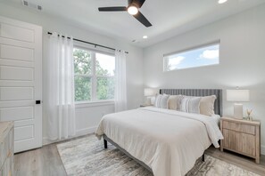 Une chambre à coucher avec un lit, des tables de chevet, un ventilateur de plafond et une fenêtre.