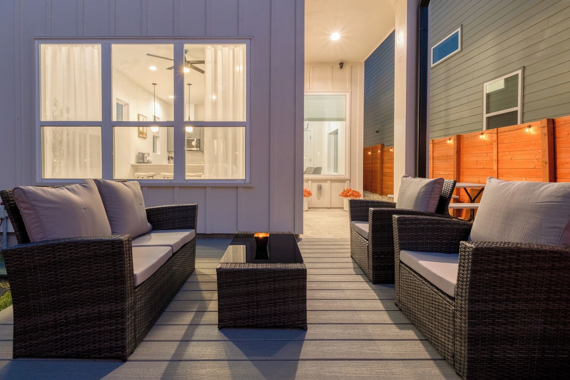 An outdoor patio with wicker furniture, a glass-top table, and a view of the interior.
