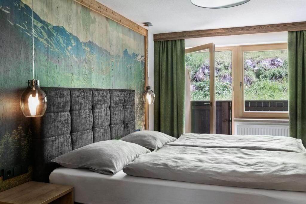 Un dormitorio con una cama grande, un cabecero, una lámpara de pared y un ventanal con cortinas.