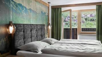 Un dormitorio con una cama grande, un cabecero, una lámpara de pared y un ventanal con cortinas.