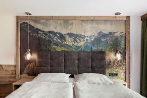 A double bed with a headboard, two bedside lamps, and a large wall mural of a mountain landscape. - Berggasthaus Höllensteinhütte (Tux)