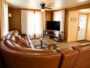 Ein Wohnzimmer mit einem braunen Ledersofa, einem Fernseher, einem Couchtisch und einem Deckenventilator.