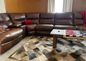 Ein braunes, ledernes Ecksofa mit einem roten Kissen, einem Holztisch und einem gemusterten Teppich.