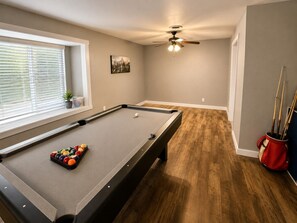 A pool table with balls, a ceiling fan, and a window with blinds. - Crew-Friendly 4BR Retreat | Sleeps 8+ | Fast WiFi (Gainesville)