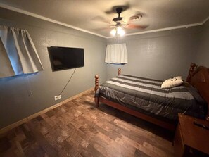 A bedroom with a bed, a ceiling fan, a mounted TV, and a wooden floor. - Crew-Friendly 4BR Retreat | Sleeps 8+ | Fast WiFi (Gainesville)