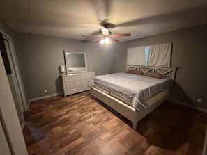 Ein Schlafzimmer mit einem Bett, einer Kommode, einem Deckenventilator und einem Fenster mit Vorhängen.