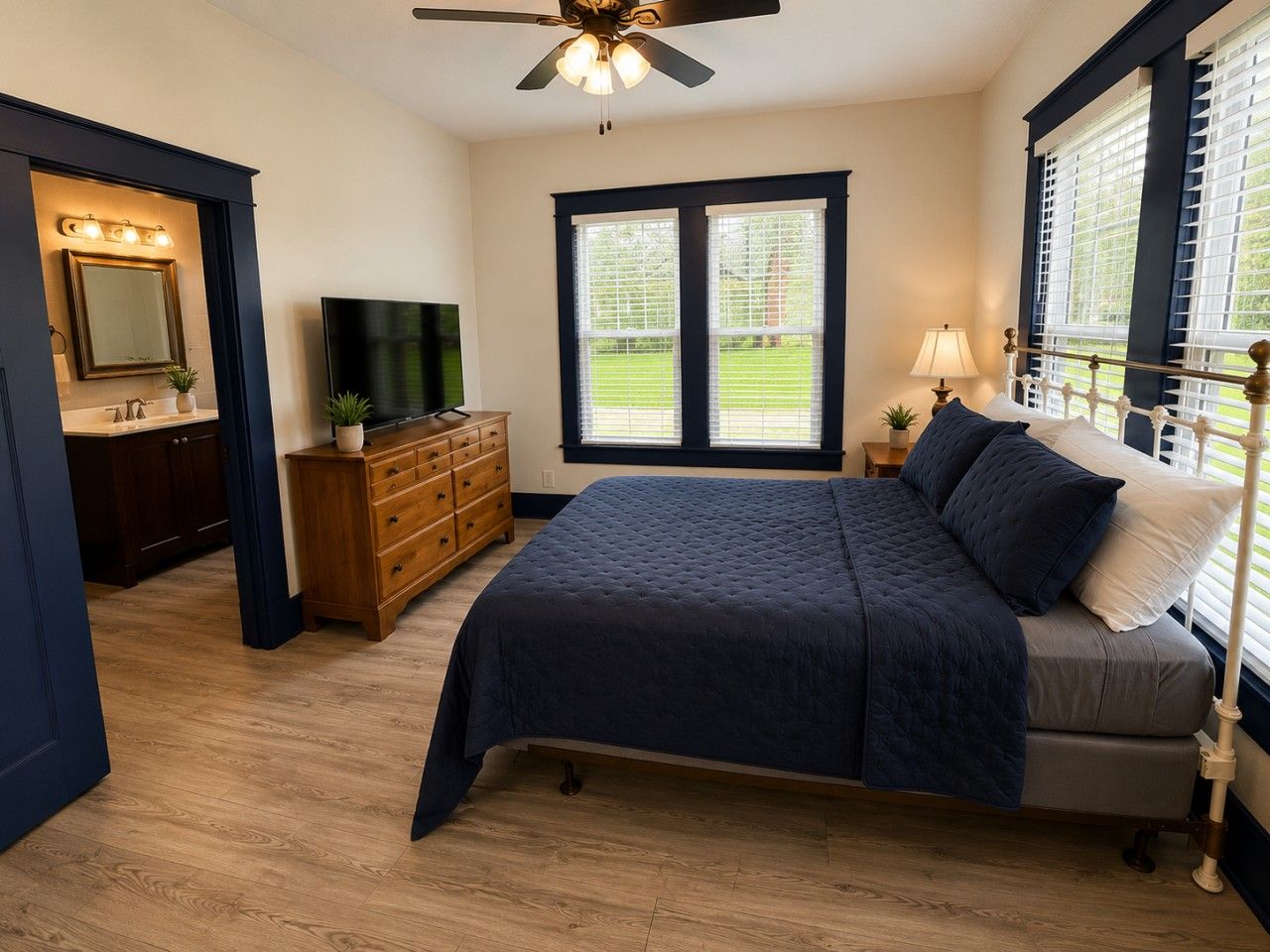 A bedroom with a bed, a dresser, a television, and a window with blinds.