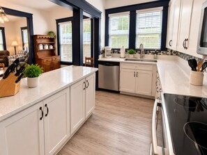 A modern kitchen with white cabinetry, a central island, and a built-in stove. - Built for Work Crews & Extended Business Stays. (Gainesville)