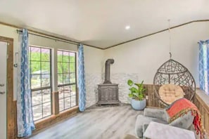 Quarto com lareira de pedra, cadeira suspensa e grande janela com cortinas.