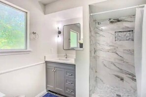 A bathroom with a window, a sink, a mirror, and a shower with marble walls. - 2 Lakefront Luxury Homes, Private Dock & Firepit (Quinlan)