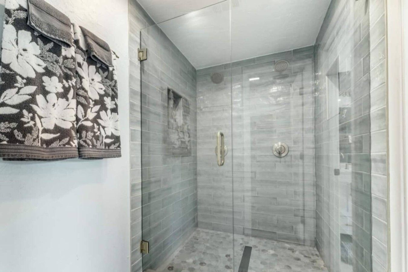 Une douche fermée par des parois de verre, avec un sol carrelé et un porte-serviettes mural orné d’un motif floral.