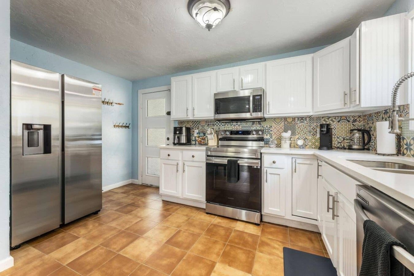 A modern kitchen with stainless steel appliances, white cabinetry, and a patterned backsplash.