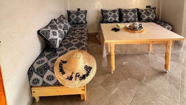 Une pièce avec une table en bois, deux canapés à motifs, un panier en osier et un luminaire suspendu au plafond.