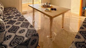 Une pièce avec un canapé à motifs, une table avec une théière et des verres, un ventilateur de plafond, un appareil de climatisation et une vue à travers une porte coulissante.