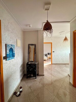 A hallway with a tiled floor, a wooden door, a mirror, and a hanging light fixture. - Beachfront Apartment in Saidia (Saïdia)