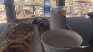 Une table avec une assiette de nourriture, un verre et une vue sur la plage et l’océan par la fenêtre.
