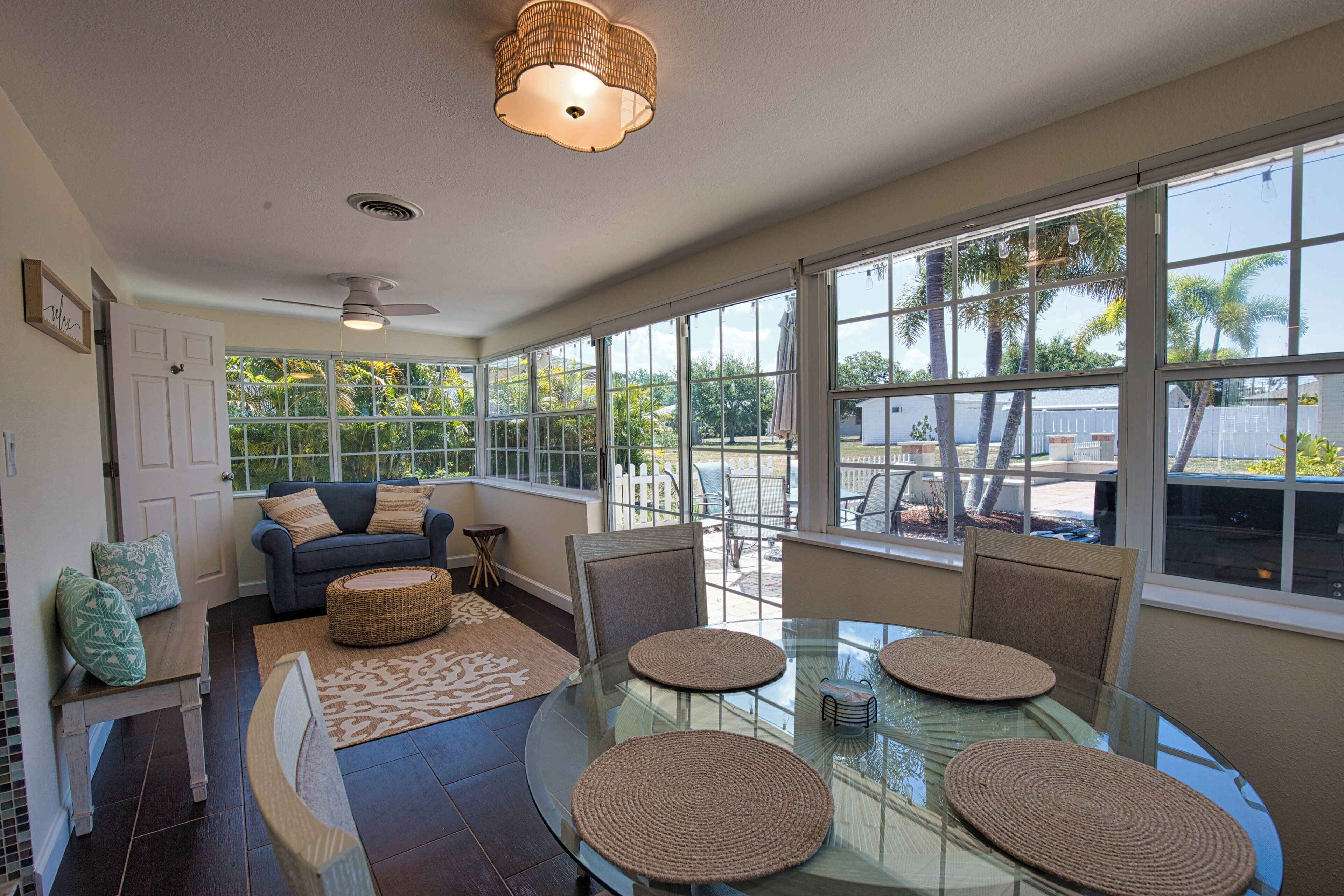 A spacious living room with a glass dining table, comfortable seating, and large windows offering a view of the outdoors.