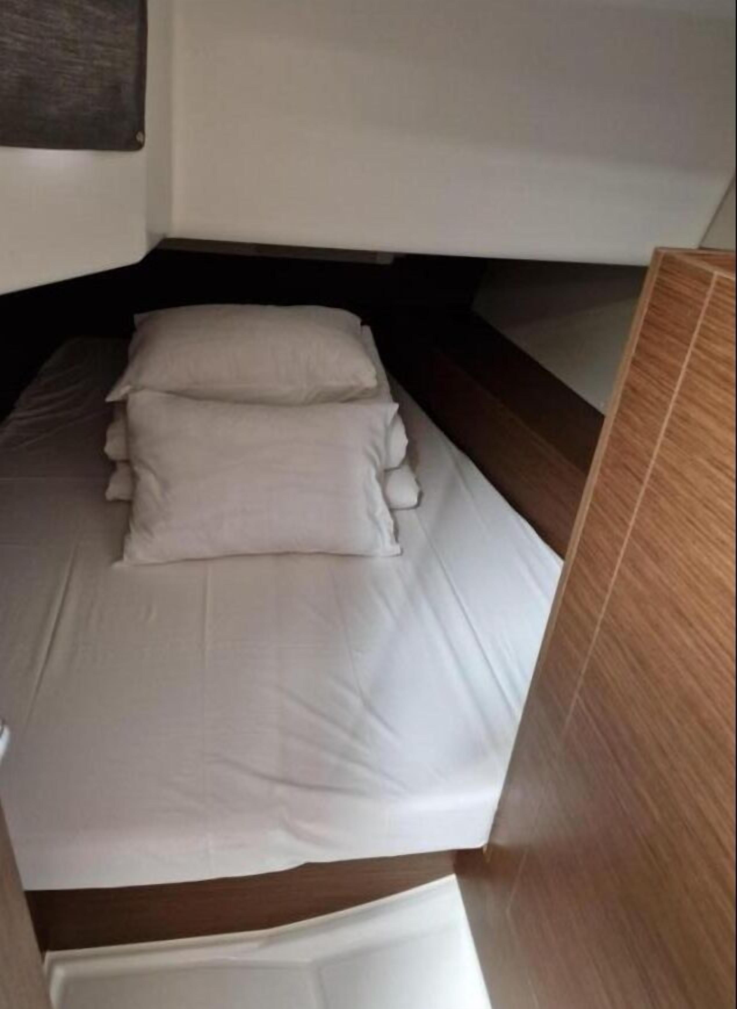 A small, narrow room with a bed, a wooden headboard, and a wooden floor.
