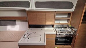 Pieni, käytännöllinen keittiö, jossa on pesuallas, liesi ja säilytystilaa tarjoavat kaapit.