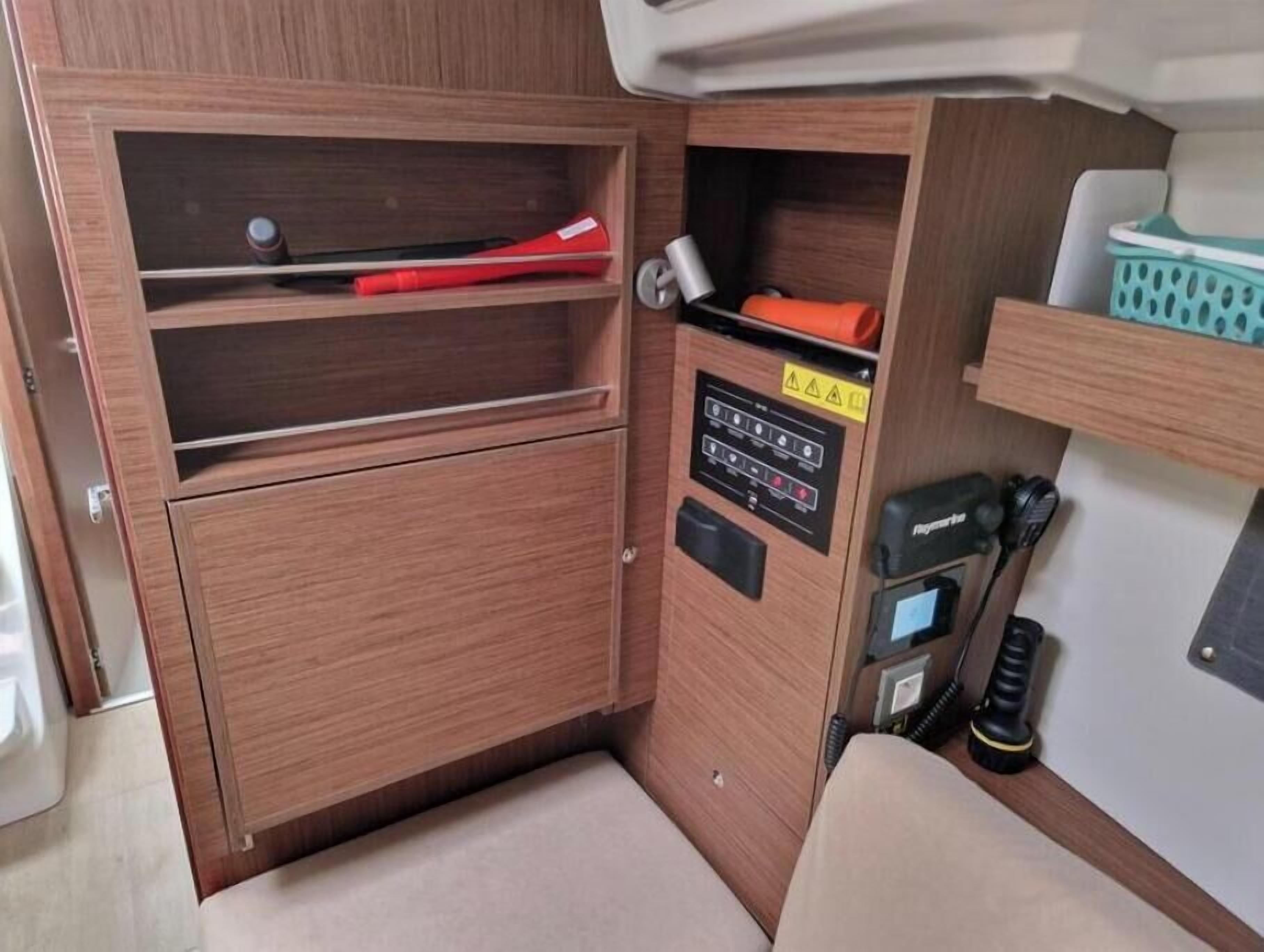 A compact storage area with wooden cabinetry, a control panel, and a small seating area.