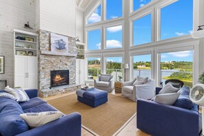 A spacious living room with a stone fireplace, large windows, and a view of a lake.