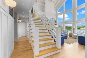 A spacious interior with a wooden staircase, large windows, and a view of the outdoors.