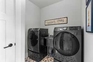 A laundry area with two front-loading washers and dryers, a 'General Store' sign, and patterned floor tiles.