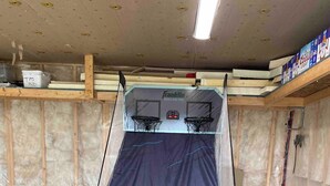 A basketball hoop with a net, a trash can, and a storage shelf with a box labeled 'TPO.' - Escape to The Blue Bird – a cozy 2-bedroom cottage with hot tub and partial ocean views! Just 5 mins from Carbonear & 15 mins to Salmon Cove Sands. (Flat Rocks)