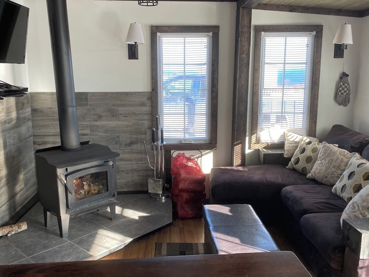 A cozy living room with a wood-burning stove, a sofa, and a window with blinds.