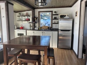 Eine moderne Küche mit weißen Schränken, einem Edelstahl-Kühlschrank, Holzböden und einem Esstisch mit Bänken.