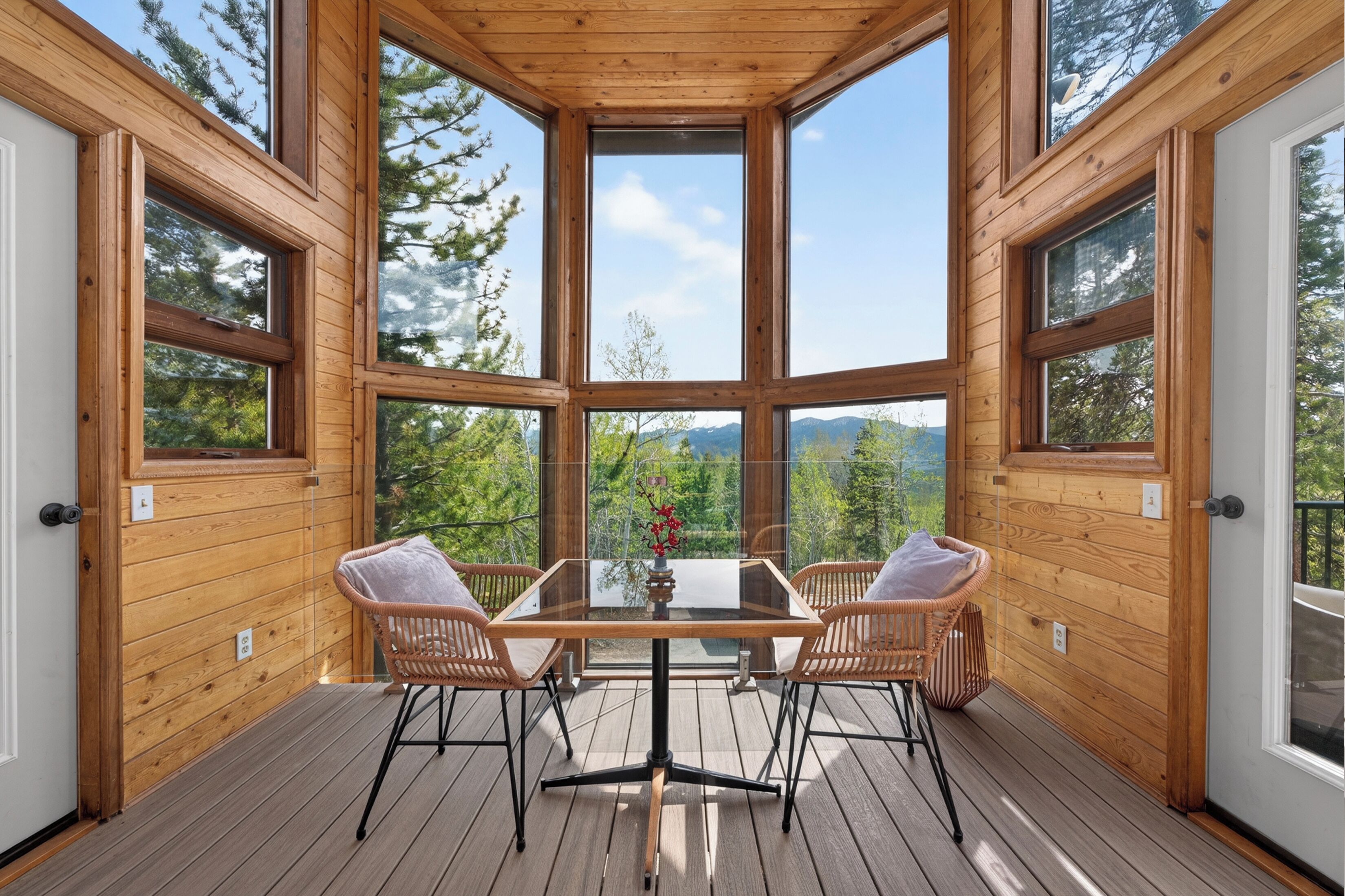 Une terrasse en bois avec une table en verre et des chaises en osier, offrant une vue sur un paysage montagneux.