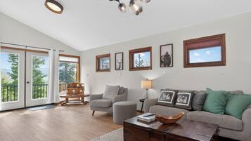 A spacious living room with a sofa, armchair, and coffee table, a wooden chest, and a chandelier.