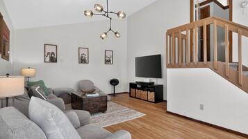 A modern living room with a sofa, a coffee table, a TV stand, and a staircase.