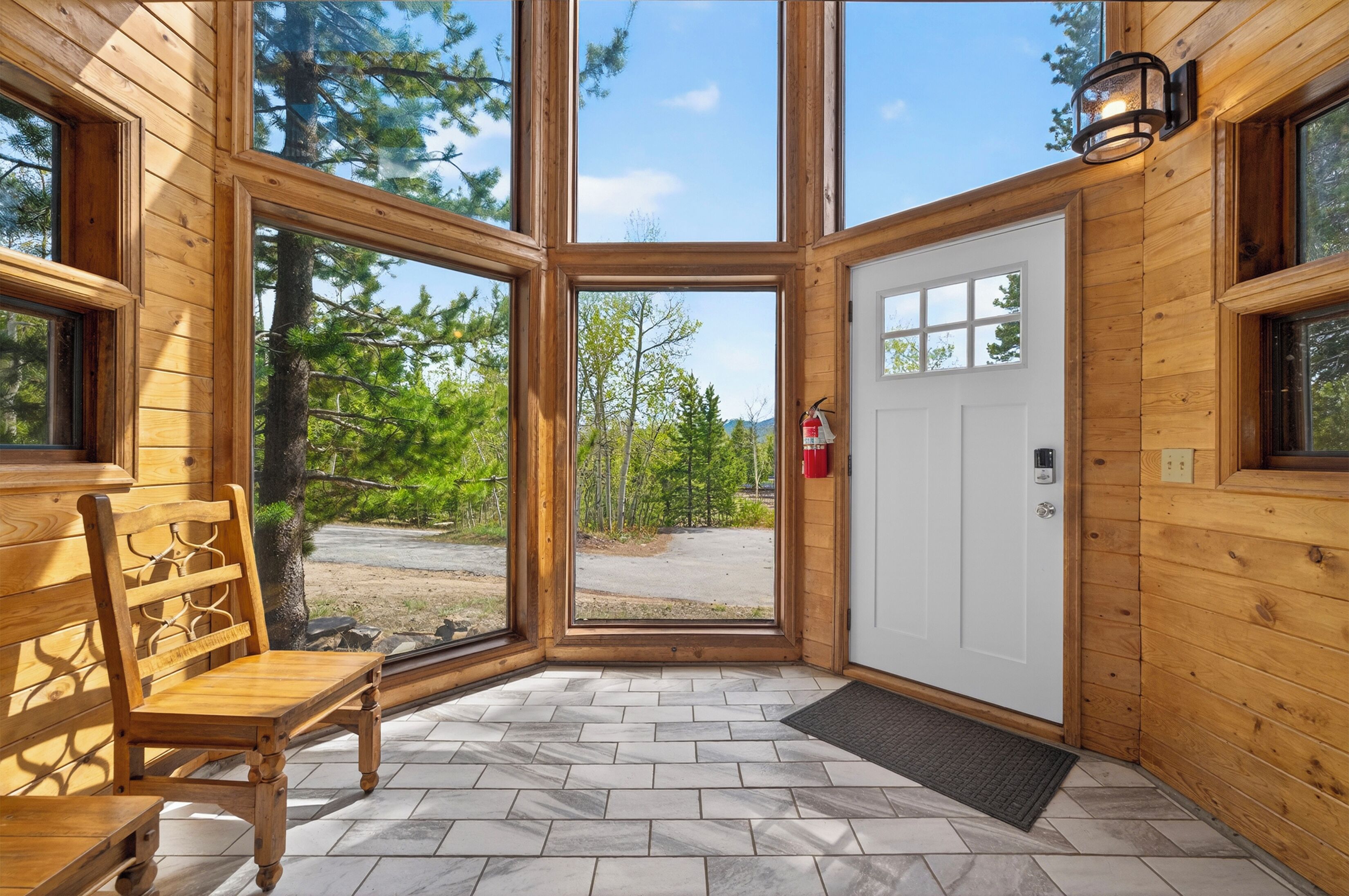 Eine Holzhütte mit einer großen Glasdoor, die zu einer Veranda führt, einer Bank und einem an der Wand befestigten Feuerlöscher.
