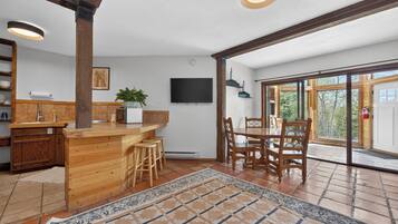 A kitchen with wooden cabinetry, a bar area, a dining table with chairs, a TV mounted on the wall, and a large sliding glass door leading to an outdoor area.