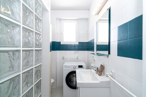 A compact bathroom with a washing machine, a sink, and a glass shower enclosure. - Apartment in Nerja Near Carabeillo Beach (Nerja)