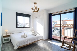 A hotel room with a bed, a nightstand, a lamp, a window, and a view of the city. - Apartment in Nerja Near Carabeillo Beach (Nerja)