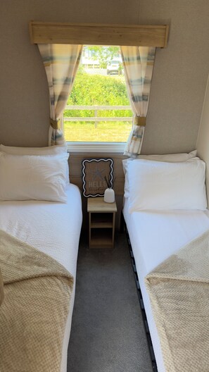 A room with two beds, a small table with a decorative item, and a window with curtains. - LITTLE SEA (Weymouth)