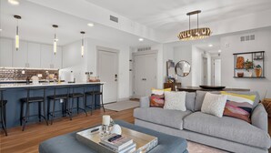 Eine moderne Küche mit Barhocker, ein Essbereich mit einer Couch und ein Wohnzimmer mit Couchtisch.
