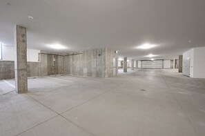 Un vaste parking souterrain, vide, avec des piliers et des murs en béton, et une porte de garage au fond.