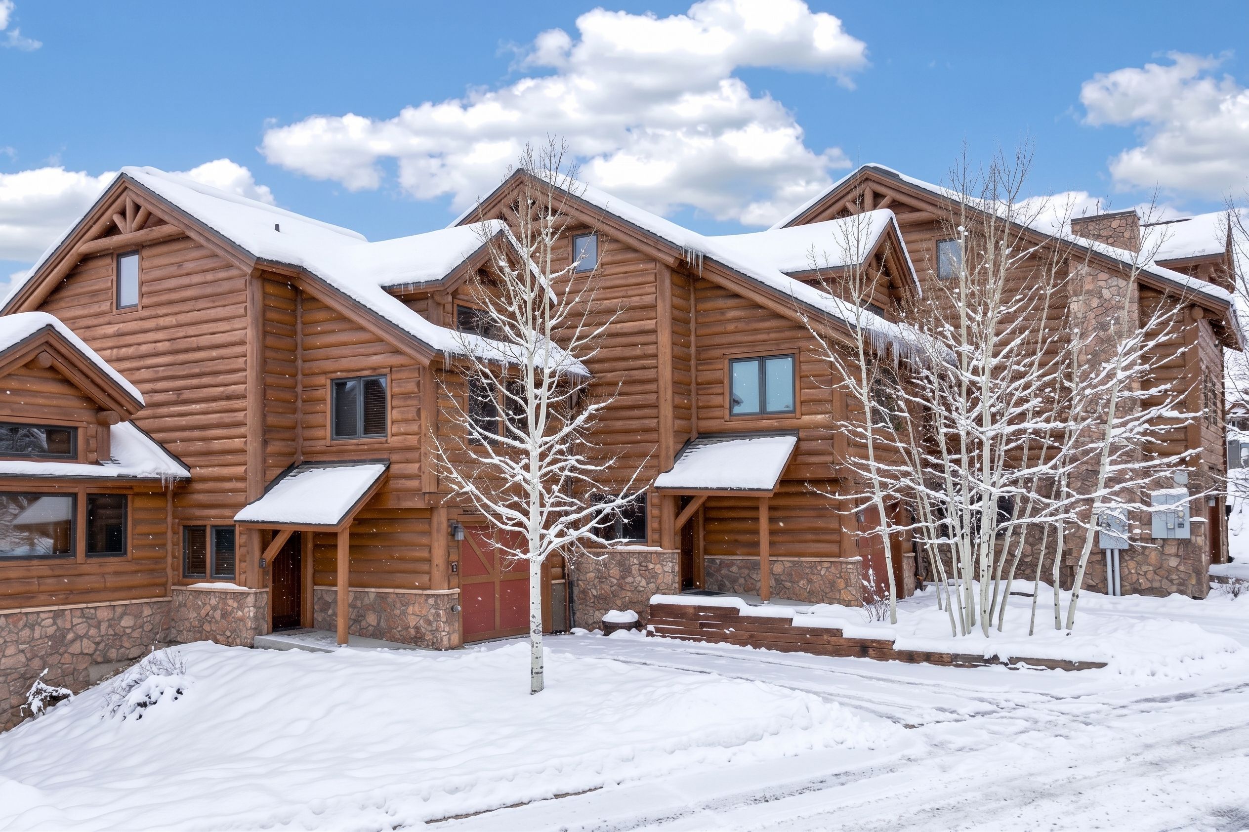 A multi-story log cabin with a stone foundation, snow-covered roof, and a clear sky.