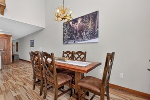 Ein Essbereich mit einem Holztisch und Stühlen, einer Kristalllüster und einem gerahmten Gemälde von Wildtieren an der Wand.