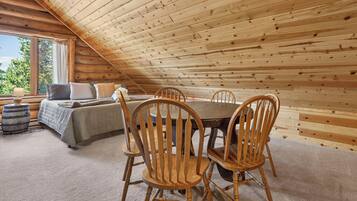 A cozy attic bedroom with a wooden sloped ceiling, a bed with pillows, a small table, and chairs.