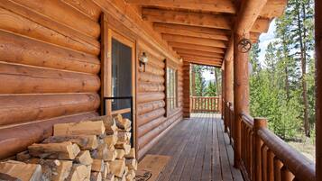 Une cabane en bois avec un porche, une porte et une pile de bois de chauffage.